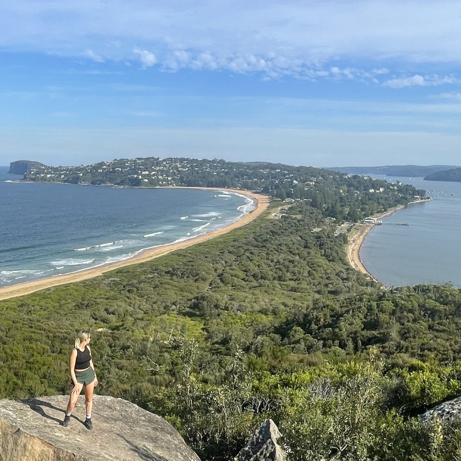 Person standing on a rocky outcrop overlooking a coastal landscape with a beach and ocean.